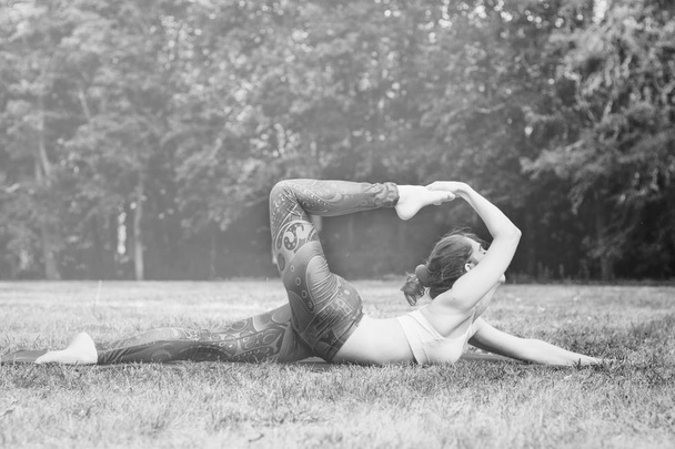schlanke junge Frau beim Stretching in der Natur. im Gras liegend mit einem gestreckten Bein und Arm. gutes gesundes und sportliches Konzept. Kopierraum für Text mit abgemilderter Wirkung. Schwarz-Weiß-Foto. Seitenansicht - Foto, Bild