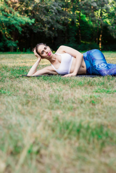 自然の中でヨガの練習にスリムな若い女性。緑の草の上に横たわると、笑顔します。緑の背景。良好な健康とスポーツ コンセプト。コピーのテキストのための領域. - 写真・画像