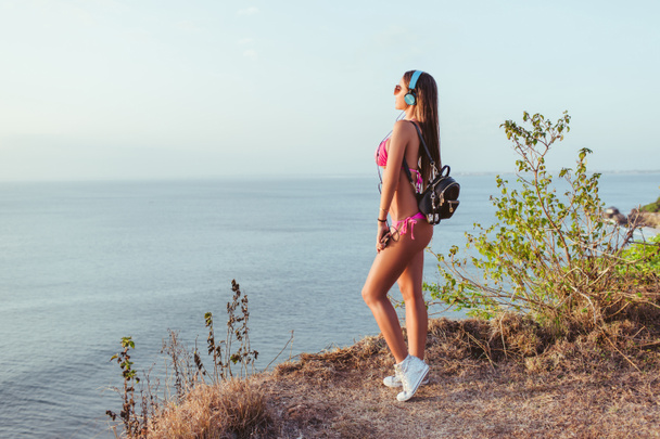 side view of attractive girl in pink bikini and headphones looking at ocean at beach - Fotó, kép