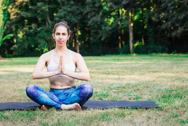 Mladá žena cvičí jóga v přírodě. Sedí na zelené trávě a meditovat. Zelené pozadí s tónovaný účinkem. Zdravá a sportovní koncept. Kopírovat prostor pro text. - Fotografie, Obrázek