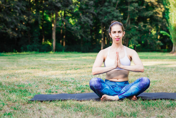 Молодая женщина практикует йогу на природе. Зеленый фон с тонизирующим эффектом. Здоровое и спортивное мышление
. - Фото, изображение