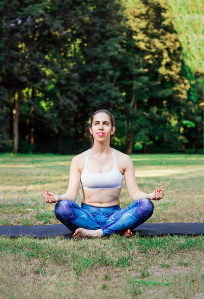 Mujer joven practicando yoga en la naturaleza. Sentada sobre hierba verde y meditando. Fondo verde con efecto tonificado. Concepto saludable y deportivo.Copiar espacio para texto
. - Foto, imagen