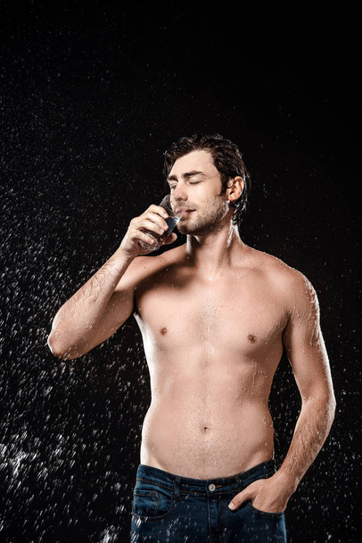 retrato del hombre sin camisa bebiendo agua de vidrio mientras se hincha con agua aislada en negro
 - Foto, Imagen