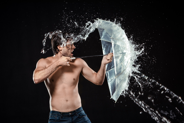 side view of shirtless man with umbrella with water splash isolated on black - Photo, Image