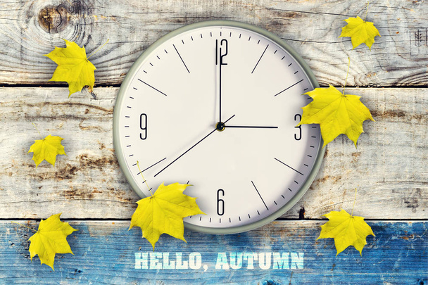 Clock and beautiful yellow autumn leaves on a wooden background. Inscription, Hello Autumn. Autumn background. - Photo, Image