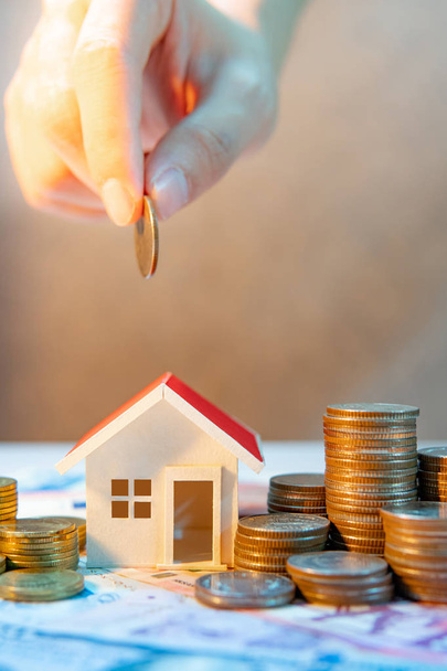 Real estate or property investment growing business. Home mortgage loan rate. Saving money for retirement concept. male hand holding coin over house model and coin stack on international banknotes - 写真・画像