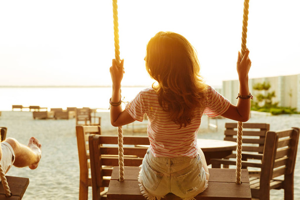 Back view image of young lady outdoors on the beach riding on swing. - Foto, Imagen