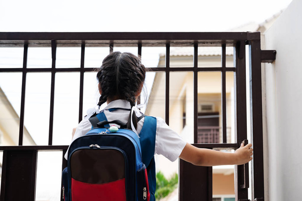 Petite fille asiatique en uniforme ouvrant la porte pour partir à l'école le matin avec sac à dos bleu
 - Photo, image