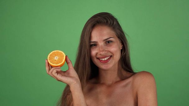 Studio shot of a gorgeous happy woman smiling holding half of an orange - Zdjęcie, obraz
