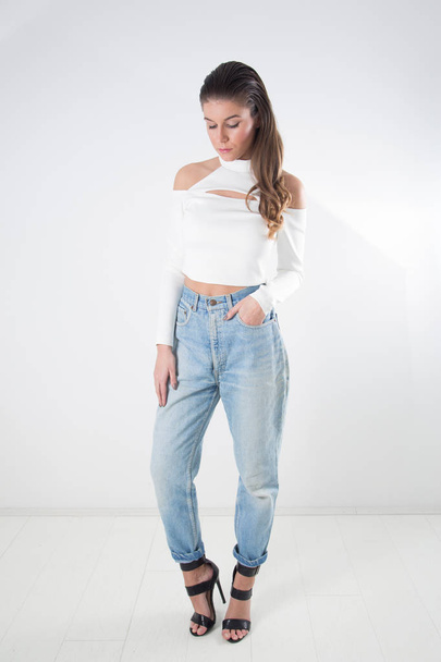 Full-Length Studio Shot Of Young Woman With Long Slicked Back Hair Wearing Jeans, White Blouse With Bare Shoulders And Black High Heeled Sandals With Straps - Photo, Image