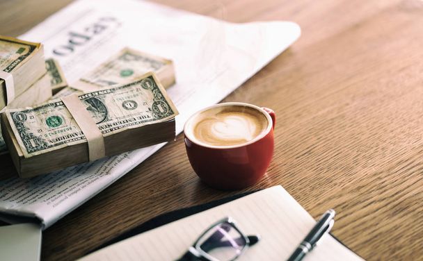 Empresario trabajando en cafetería con café, dinero, laptop, bloc de notas, periódico en mesa de madera
 - Foto, Imagen