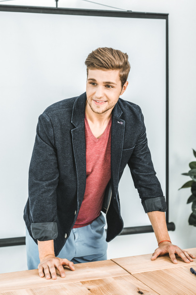 portrait of young smiling businessman leaning on table in office - Photo, Image