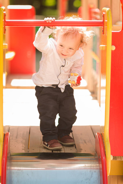 Cute baby boy playing on a slide on the playground - Fotó, kép