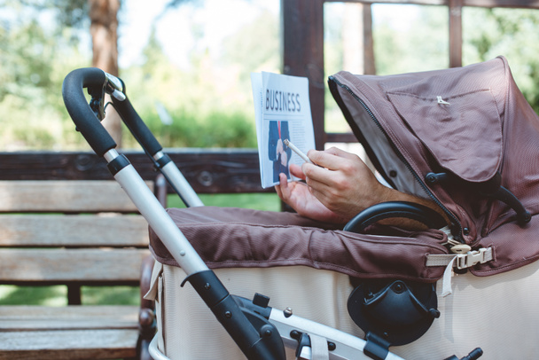 cropped image of man holding cigarette and business newspaper in baby carriage - Foto, afbeelding