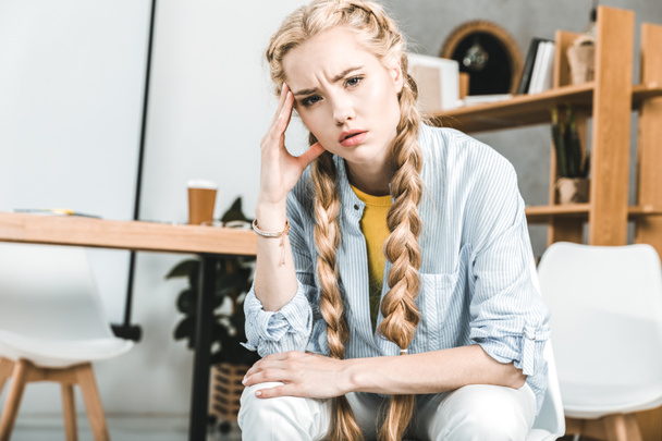 portrait of young pensive businesswoman sitting at workplace in office and looking at camera - Foto, Bild