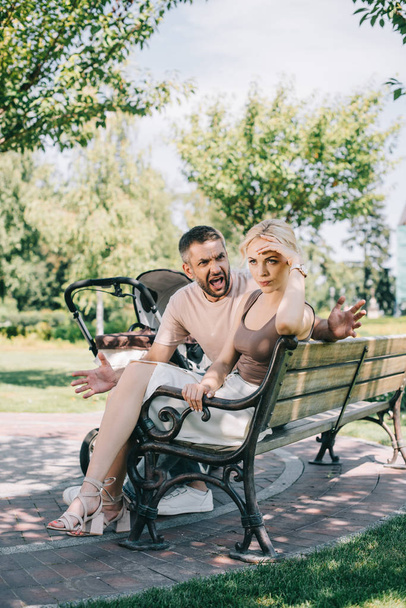 husband screaming at wife and sitting on bench near baby carriage in park  - Foto, imagen