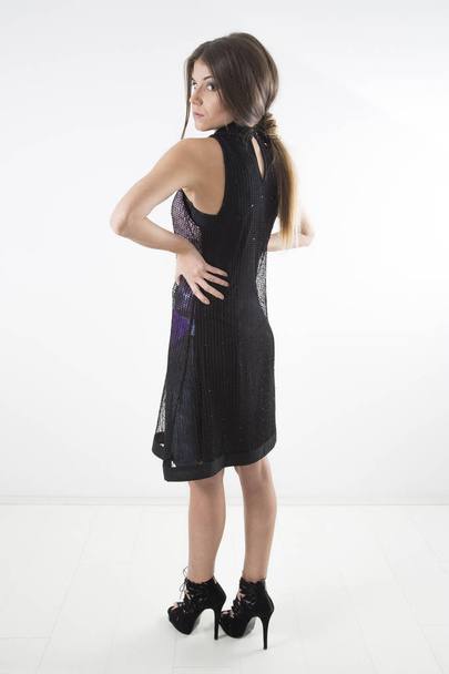 Side View Of Young Pretty Woman In Black Dress And Black High Heels Posing At Studio, Full-Length Shot Over White Background - Foto, Imagen