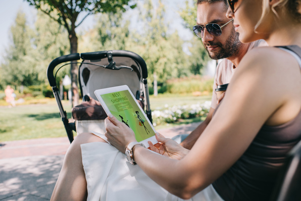 padres sentados en el banco cerca del carro del bebé y mirando la tableta con la mejor página de compras
 - Foto, imagen