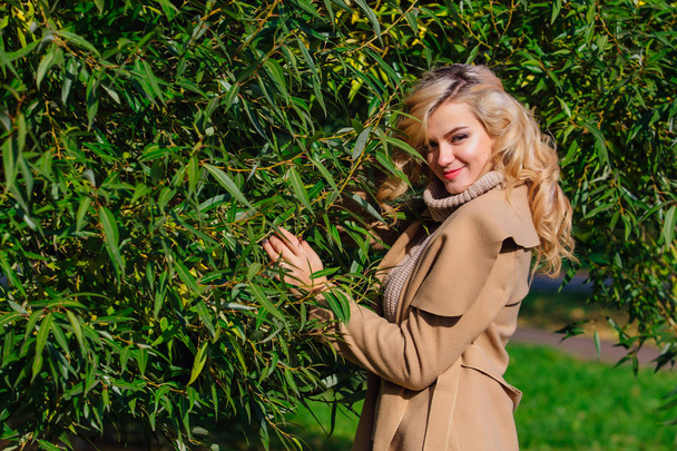 Beautiful elegant blonde woman dressed in a coat standing under the tree in autumn park. Sunny october day. - Φωτογραφία, εικόνα