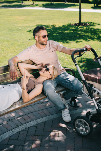 esposa acostada en piernas de marido cerca de carro de bebé en el parque
 - Foto, imagen