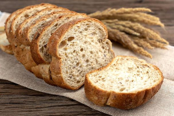 Sliced bread with sunflower seeds and sesame on sack. Fresh Homemade Whole Wheat Bread on wooden table. - Photo, Image