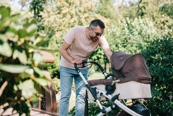 smiling father looking at baby carriage in park - Foto, Imagem