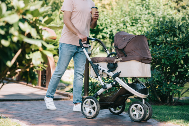 cropped image of father walking with baby carriage and disposable coffee cup in park - Foto, Imagen