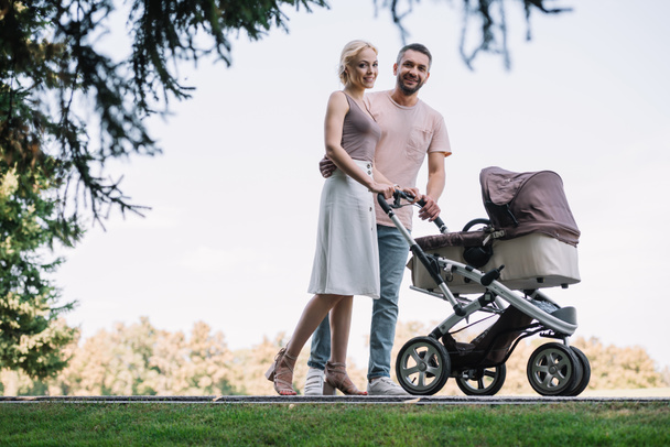 happy parents walking with baby carriage in park - Fotó, kép