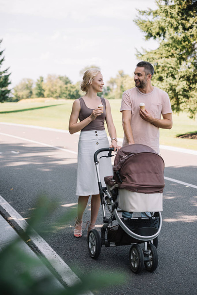 smiling parents walking with baby carriage and ice cream in park - Fotó, kép