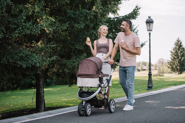 happy parents walking with baby carriage and ice cream in park - Fotoğraf, Görsel