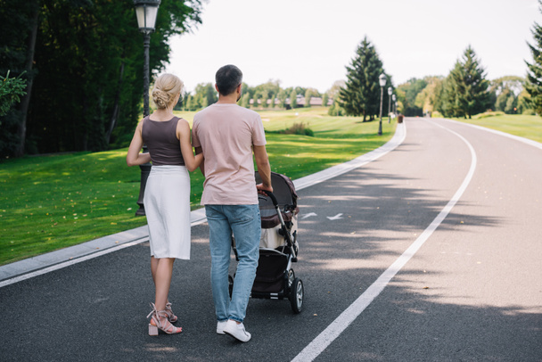 back view of parents walking with baby carriage on road in park - Foto, Imagen