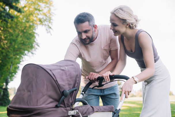 cheerful parents looking at baby carriage in park - Foto, immagini