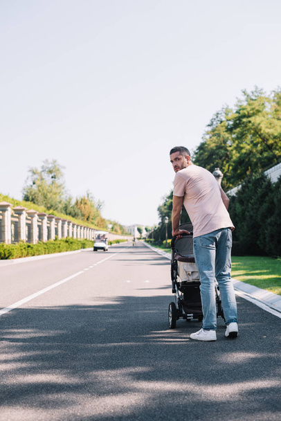 back view of father walking with baby carriage on road in park - Photo, Image