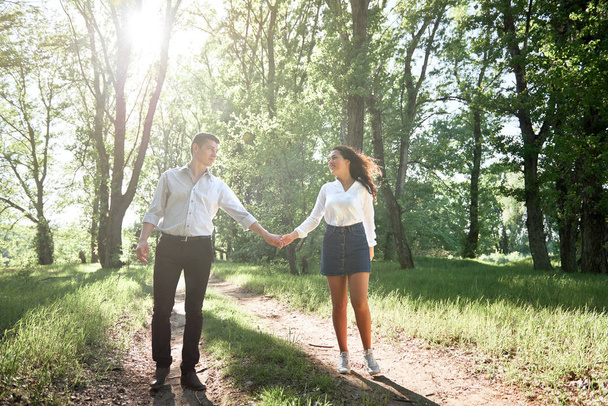 young couple walking in the forest, summer nature, bright sunlight, shadows and green leaves, romantic feelings - Фото, зображення