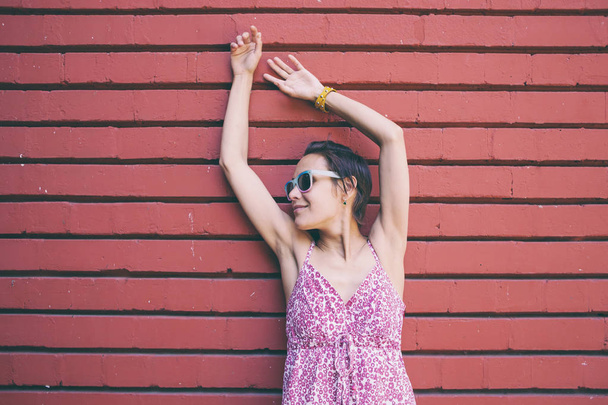 Mujer delgada en un vestido sobre un fondo de pared de ladrillo rojo. Chica sonriente con gafas. Una hermosa morena camina por una calle de la ciudad
. - Foto, imagen