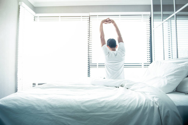 Homem acorda e se estende na cama de manhã com a luz do sol
 - Foto, Imagem