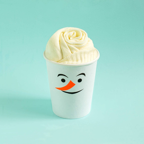 Socks in paper cup, hand-decorated with snowman applique on blue background. Imitation of festive cocktail. Minimal style. Creative idea, imagination and fantasy. Christmas and New Year concept - Photo, Image
