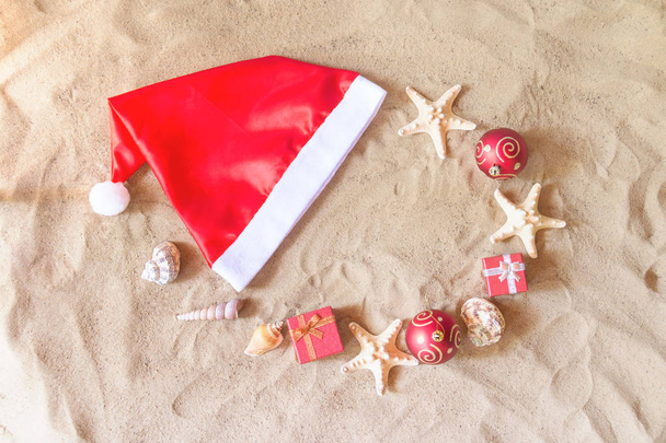 Шляпа Санта-Клауса, рождественские балы, подарки, ракушки и морские звезды на песчаном пляже
 - Фото, изображение