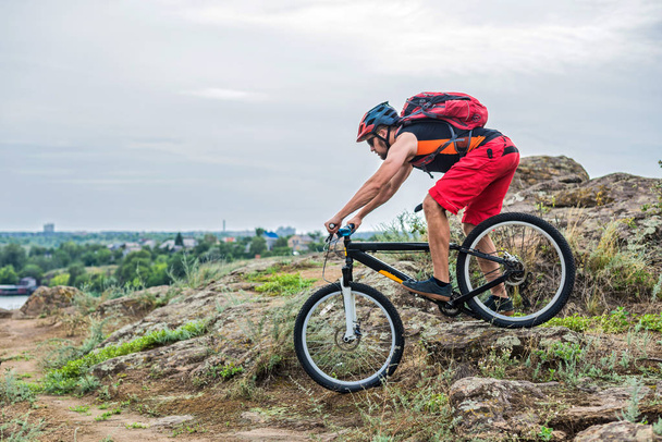 Cyclist riding down the rock on a mountain bike, extreme enduro cycling. Cyclist in a helmet and with a backpack on a blue sky background, free space. - Photo, Image