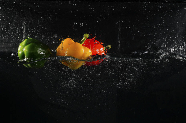 several coloured paprika falling into water splash with many bubble - Foto, Bild