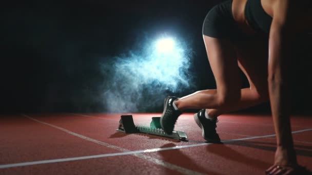 Genç kadın atlet siyah şort ve tişört start çizgisinde yakınındaki koşu bandı üzerinde 100 metre yarışında başlatmak hazırlanıyor - Video, Çekim