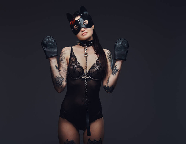 Sexy vrouw dragen zwarte lingerie in Bdsm kat lederen masker en accessoires poseren op een donkere achtergrond.  - Foto, afbeelding