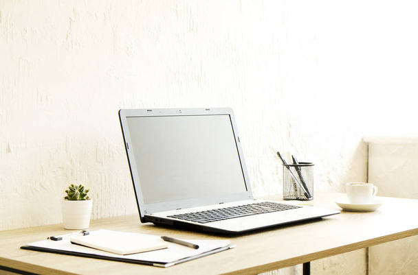 Ordenador portátil de pantalla en blanco, taza de café capuchino, cactus, suministros y gafas plegadas en escritorio de madera en una espaciosa oficina llena de luz solar. Espacio de trabajo creativo. Cerrar, copiar espacio, fondo
 - Foto, imagen