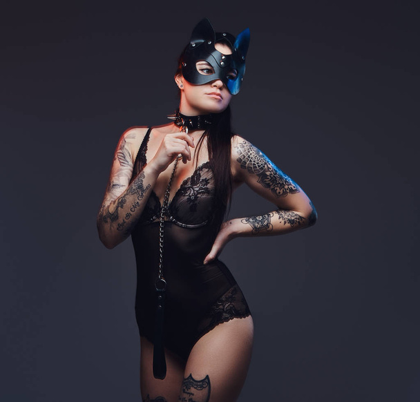 Seductora sensual amante chica con lencería negra en accesorios BDSM y máscara de cuero para gatos posando sobre un fondo oscuro. Aislado sobre un fondo oscuro
.    - Foto, Imagen