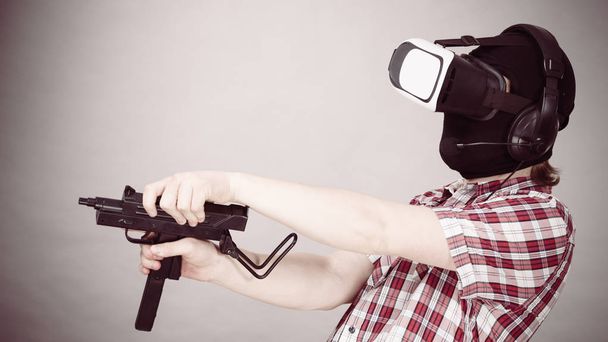 Man playing video game wearing virtual reality device holding gun. Gaming equipment for gamers concept. - Photo, image