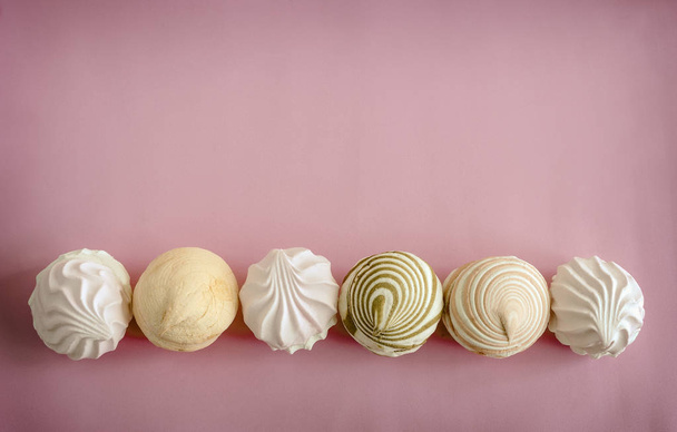 Marshmallows verschiedener Sorten werden in einer Zeile auf rosa Hintergrund präsentiert. Der Blick von oben. - Foto, Bild