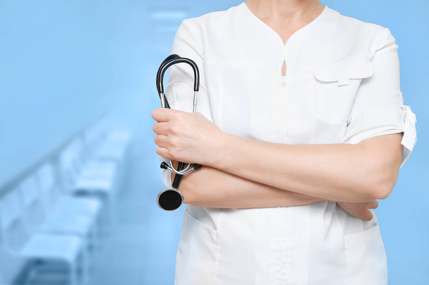 Woman doctor with stethoscope in hand on blue background of clinic. Close-up. - Foto, afbeelding