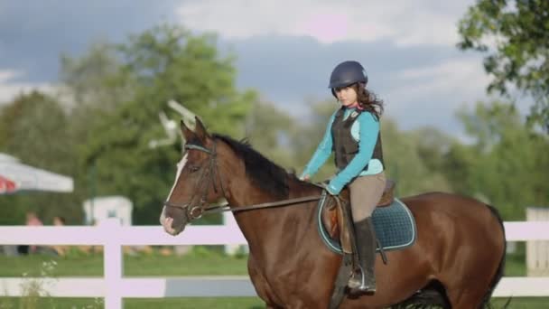 MOTION DE LENT FERMER : Jeune fille à cheval belle jument châtaignier dans l'arène d'équitation en plein air pendant les vacances d'été ensoleillées. Cheval avec un enfant cavalier trottant dans un manège sablonneux à l'intérieur du corral
 - Séquence, vidéo