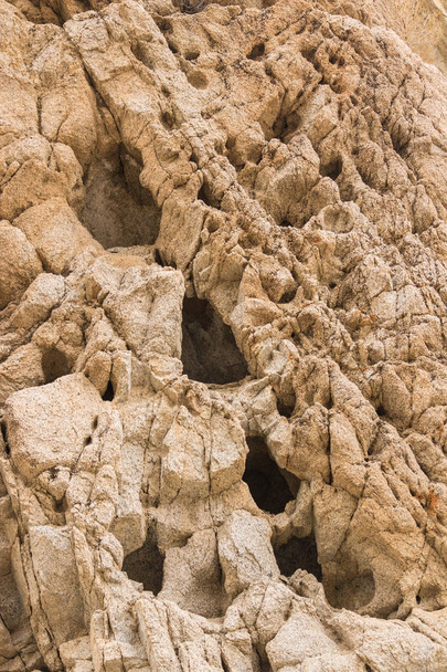 Primer plano de la pared de roca del desierto con agujeros oscuros profundos y grietas en la superficie, formato vertical
 - Foto, imagen