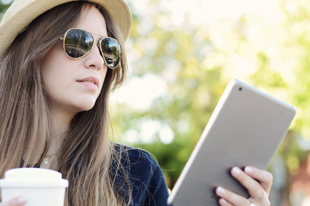 Портрет молодої красивої жінки, яка використовує свій планшет з чашкою кави. На відкритому повітрі. Міська сцена
. - Фото, зображення